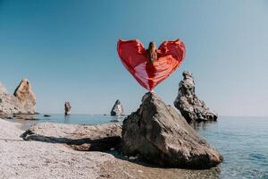 vrouw reizen zee. jong gelukkig vrouw in een lang rood jurk poseren Aan een strand in de buurt de zee Aan achtergrond van vulkanisch rotsen, Leuk vinden in IJsland, sharing reizen avontuur reis foto