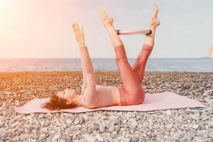 vrouw zee pilates. sportief gelukkig midden- oud vrouw beoefenen geschiktheid Aan strand in de buurt zee, glimlachen actief vrouw opleiding met ring Aan yoga mat buiten, genieten van gezond levensstijl, harmonie en meditatie foto