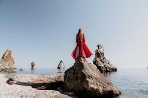 vrouw reizen zee. jong gelukkig vrouw in een lang rood jurk poseren Aan een strand in de buurt de zee Aan achtergrond van vulkanisch rotsen, Leuk vinden in IJsland, sharing reizen avontuur reis foto