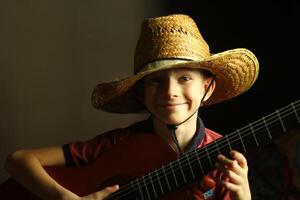 portret van een Kaukasisch jongen vervelend een rietje hoed en spelen de gitaar foto