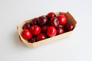 een kers met druppels van water leugens Aan een wit keuken tafel in een houten dienblad. rustiek fruit achtergrond foto