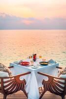 zeegezicht visie onder zonsondergang licht met dining tafel met oneindigheid zwembad in de omgeving van. romantisch rustig ga weg voor twee, paar concept. stoelen, voedsel en romantiek. luxe bestemming dineren, huwelijksreis sjabloon foto