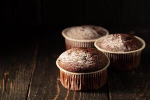 chocola muffins met gepoederd suiker Aan een zwart achtergrond. nog steeds leven dichtbij omhoog. donker humeurig. voedsel foto. foto