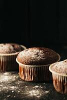 chocola muffins met gepoederd suiker Aan een zwart achtergrond. nog steeds leven dichtbij omhoog. donker humeurig. voedsel foto. foto