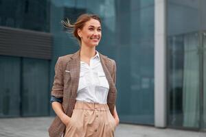 blond zakenvrouw glimlacht en looks weg. tegen de achtergrond van een groot bedrijf centrum. blouse en elegant pak. foto