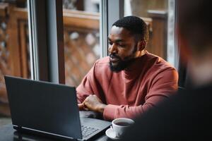 Afrikaanse Amerikaans Mens werken Aan laptop in een cafe. foto