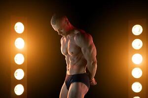 actief levensstijl concept. professioneel bodybuilder tonen perfect gespierd lichaam, lampen verlichting Aan achtergrond foto