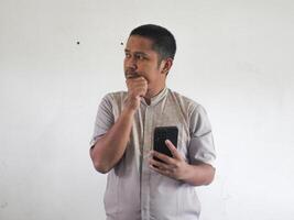 Aziatisch Mens Holding zijn mobiel telefoon met echt uitdrukking foto