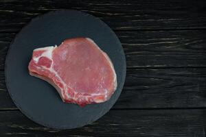 top visie van een stukken rauw varkensvlees karbonade steaks Aan een zwart steen snijdend bord. foto