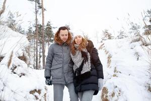 een jong stel, een Mens en een vrouw zijn wandelen in een winter met sneeuw bedekt Woud. winter vrije tijd. reizen samen. liefde zullen warm in ieder vorst foto