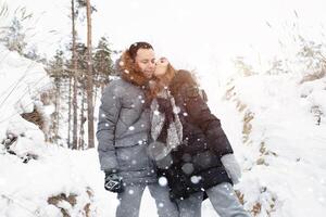 een jong stel, een Mens en een vrouw zijn wandelen in een winter met sneeuw bedekt Woud. winter vrije tijd. reizen samen. liefde zullen warm in ieder vorst foto