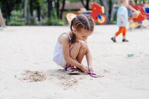 weinig meisje spelen zandbak speelplaats graven zand Schep gebouw zand figuur zomer dag foto