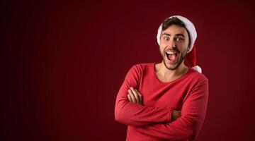 jong knap Kaukasisch vent in rood trui en de kerstman hoeden staat Aan rood achtergrond in studio en tanden glimlachen foto