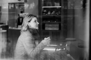 vrouw verloren in gedachte met koffie - sereen moment van reflectie Bij cafe venster - knus sfeer met vrouw genieten van stil overpeinzing over- koffie foto