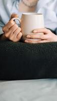 vrouw genieten van thee Aan leven kamer bank, bijgesneden visie. knus huiselijk tafereel. jong vrouw tot rust komen met thee in leven kamer interieur. vrouw handen Holding een mok met thee of koffie. detailopname foto