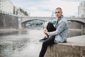 sereen moment. Mens in blauw jasje zittend door water's kant, overweegt - vredig waterkant tafereel met kalmte atmosfeer - rustig waterkant visie, ontspanning en overpeinzing concept foto