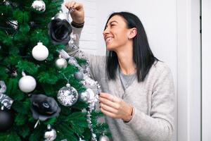 een jong vrouw versieren de Kerstmis boom, voorbereidingen treffen voor de nieuw jaar viering foto