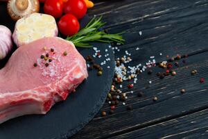 top visie van een stukken rauw varkensvlees karbonade steaks met Aan een zwart steen snijdend bord. foto