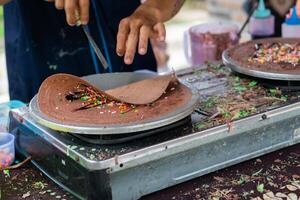 maken van pannenkoeken pannekoeken met chocola en chocola rijst- in Open markt festival eerlijk. een hand- is maken pannenkoeken buitenshuis Aan een metaal bakplaat foto