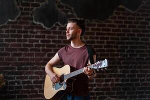 Mens met akoestisch gitaar tegen steen muur spelen muziek- het zingen liedjes genieten leven medium schieten foto