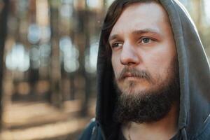 dichtbij omhoog portret van een gebaard hipster toerist in grijs kap Mens in de zonlicht bossen Woud foto