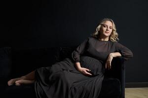 zwanger vrouw poseren in een elegant zwart jurk binnenshuis studio zwart muur achtergrond foto