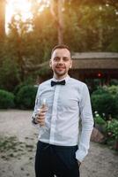een knap Mens in een wit overhemd en stropdas is proeverij wit wijn van een transparant glas. concept bedrijf diner. buitenshuis portret foto