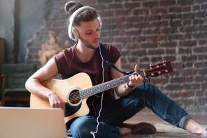 Kaukasisch jong volwassen aan het leren gitaar online muziek- klasse met ver weg leraar computer mobiel apparaat foto