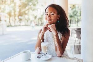 mooi Afrikaanse meisje met huid problemen en zit in een cafe voor een kop van heet thee foto