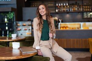 bedrijf vrouw restaurant eigenaar met laptop in handen gekleed elegant broekpak zittend Aan tafel in restaurant met bar teller achtergrond foto