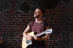 Mens met akoestisch gitaar tegen steen muur spelen muziek- het zingen liedjes genieten leven medium schieten foto