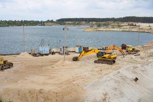 zand steengroeve mijnbouw industrie uitrusting graafmachine trekker staand zand land- in de buurt meer water foto
