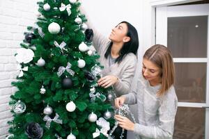 twee jong Dames versieren de Kerstmis boom, voorbereidingen treffen voor de nieuw jaar viering foto