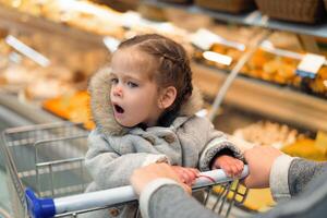 weinig meisje geopend haar mond in verrassing terwijl zittend in een supermarkt trolley foto