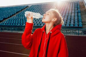 mensen, levensstijl en sport concept. sport vrouw athlet overwonnen lang afstand, drankjes water van plastic fles, luistert audio sporen in oortelefoons. foto