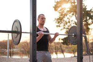 Mens met barbell buitenshuis Sportschool Aan natuur in park. foto