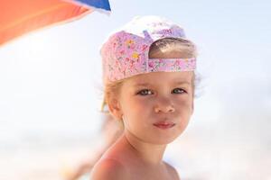 dichtbij omhoog portret weinig Kaukasisch meisje Aan strand sceptisch over op zoek Bij camera. foto