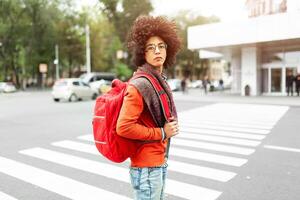 een jong Afrikaanse Amerikaans Mens met een rood rugzak kruisen de weg foto