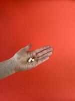 oud hand- Holding drie verschillend pillen Aan rood achtergrond. geneesmiddel, Gezondheid en behandeling concept. ideaal voor medisch en farmaceutisch fotografie foto