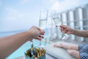 hand- paar houden Champagne bril vieren vakantie met oceaan visie. foto