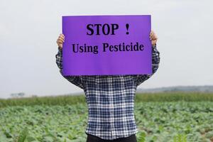 tekst hou op gebruik makend van pesticide Aan papier poster, gehouden door boer Bij tuin. concept, campagne voor roeping boeren of tuinders naar hou op gebruik makend van pesticide of chemisch met groenten. foto
