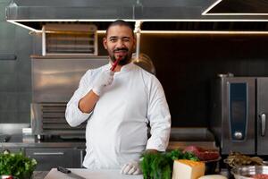 knap jong Afrikaanse chef staand in professioneel keuken in restaurant voorbereidingen treffen een maaltijd van vlees en kaas groenten. foto