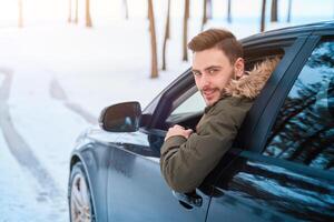 jong aantrekkelijk Kaukasisch Mens zit Bij de wiel van zijn auto zonnig winter dag. foto