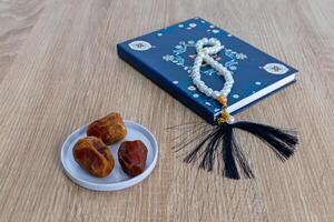 een bord van datums fruit Aan de houten tafel met een klein boek en gebed kralen foto