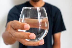 een Mens in zwart kleren Holding een glas van water foto