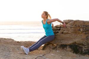 jong volwassen fit vrouw aan het doen triceps dalen opdrachten gedurende buitenshuis kruis opleiding training. geschiktheid vrouw model- opleiding zomer dag in de buurt oceaan strand. foto