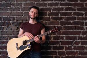 Mens met akoestisch gitaar tegen steen muur spelen muziek- het zingen liedjes genieten leven medium schieten foto