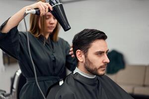 knap blauw ogen Mens zittend in kapper winkel. haar stylist kapper vrouw snijdend zijn haar. vrouw kapper. foto