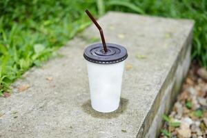 papier glas van bevroren koffie Aan beton stap verdieping met gras veld- in tropisch tuin van cafe foto