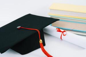 een zwart plein afstuderen hoed met een rood kwast leugens Aan een diploma en een stack van boeken. onderwijs concept foto